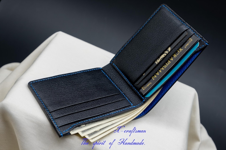 May include: A black leather wallet with blue stitching and a blue interior. The wallet is open and has several cards and cash inside.
