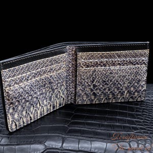 Puede incluir: Una cartera de cuero negro con un patr&oacute;n de piel de serpiente. La cartera est&aacute; abierta y muestra m&uacute;ltiples ranuras para tarjetas.
