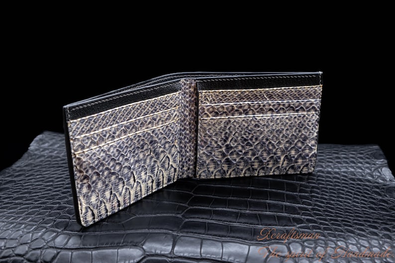 Puede incluir: Una cartera de cuero negro con un patr&oacute;n de piel de serpiente. La cartera est&aacute; abierta y muestra m&uacute;ltiples ranuras para tarjetas.