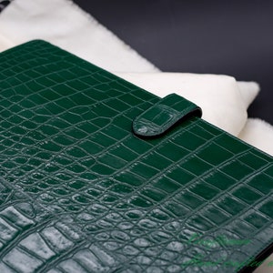 May include: A dark green leather binder with a crocodile embossed pattern and a single strap closure.