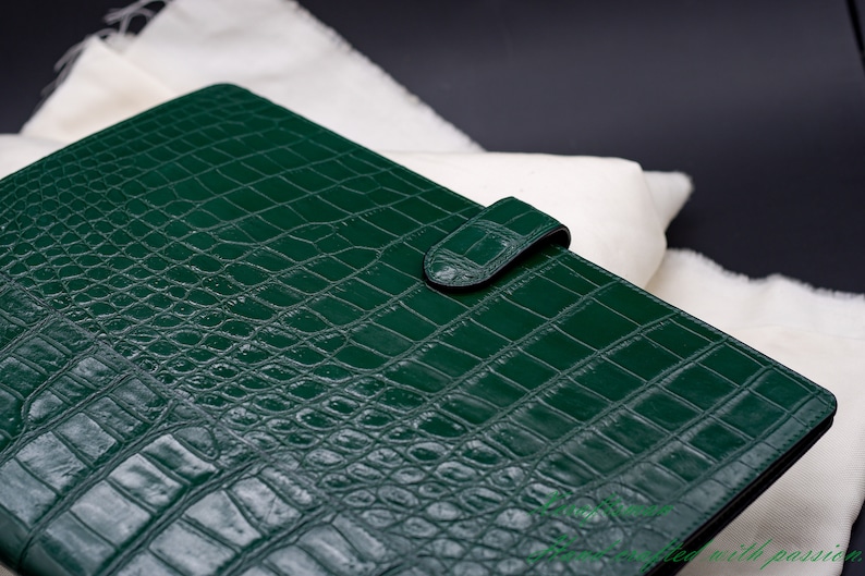 May include: A dark green leather binder with a crocodile embossed pattern and a single strap closure.