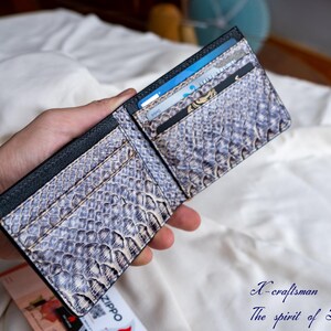 Puede incluir: Una cartera de cuero negro con un patr&oacute;n de piel de serpiente y m&uacute;ltiples ranuras para tarjetas. La cartera est&aacute; abierta y tiene varias tarjetas dentro.