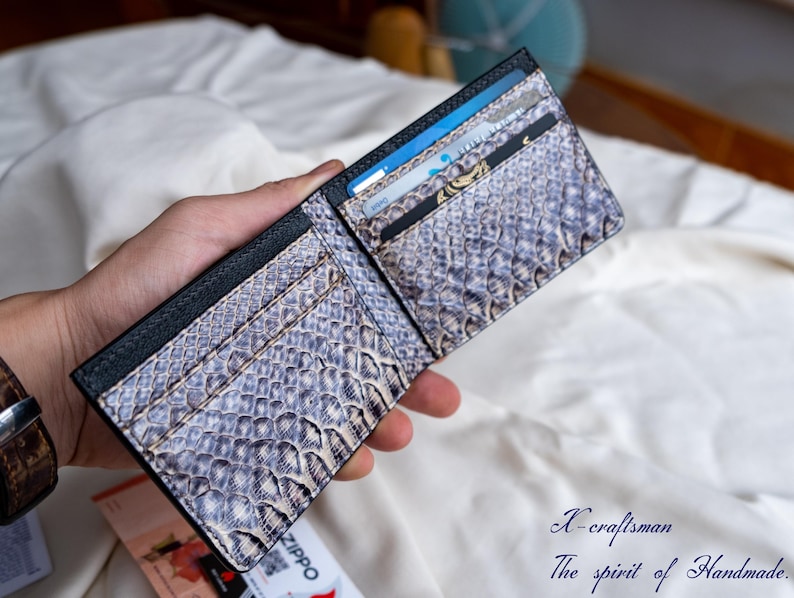 Puede incluir: Una cartera de cuero negro con un patr&oacute;n de piel de serpiente y m&uacute;ltiples ranuras para tarjetas. La cartera est&aacute; abierta y tiene varias tarjetas dentro.