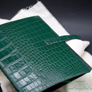 May include: A green leather binder with a crocodile embossed pattern and a black strap closure.