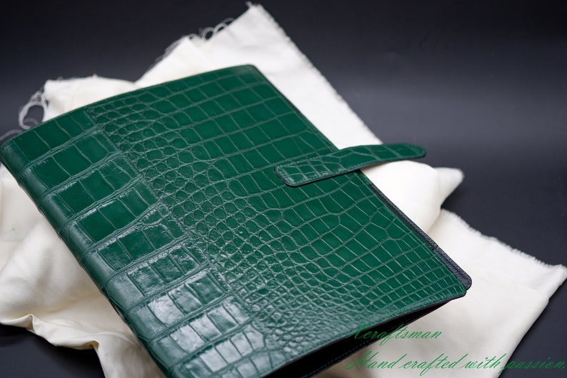 May include: A green leather binder with a crocodile embossed pattern and a black strap closure.