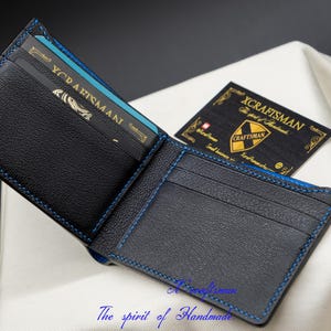 May include: A black leather wallet with blue stitching and a blue and gold card inside. The wallet is open and the inside is visible. The text "XCRAFTSMAN" is visible on a card inside the wallet.