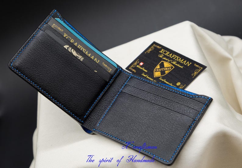 May include: A black leather wallet with blue stitching and a blue and gold card inside. The wallet is open and the inside is visible. The text "XCRAFTSMAN" is visible on a card inside the wallet.