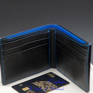 May include: Black leather wallet with blue stitching and multiple card slots. The wallet is open and a credit card is visible inside.