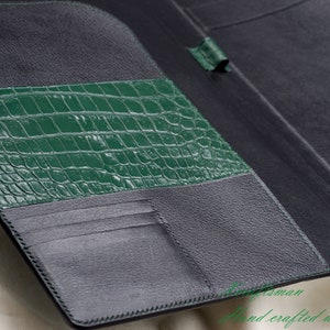 May include: A black leather wallet with a green crocodile embossed leather panel. The wallet has multiple card slots and a billfold.