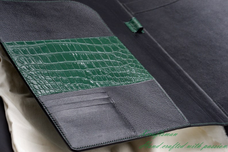 May include: A black leather wallet with a green crocodile embossed leather panel. The wallet has multiple card slots and a billfold.