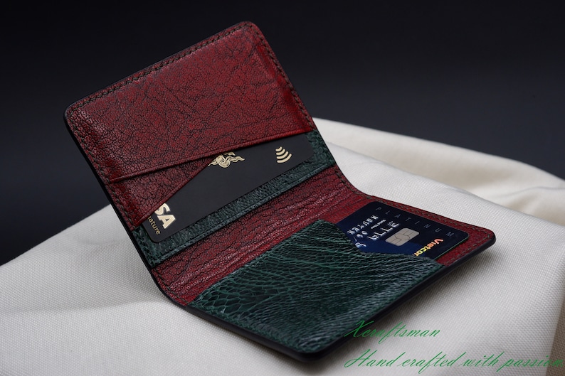May include: Open leather wallet with a textured burgundy and green interior. The wallet contains a black credit card with a gold Visa logo and a blue credit card. The words "Craftsman" and "Hand crafted with passion" are visible.