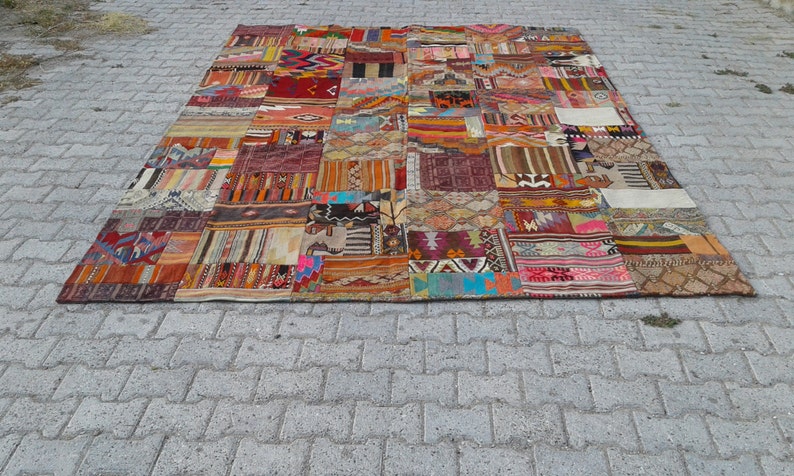 May include: A large, colorful patchwork rug made from various pieces of fabric. The rug is made up of many different colors and patterns, including red, blue, green, yellow, and brown. The rug is laid out on a gray concrete surface.