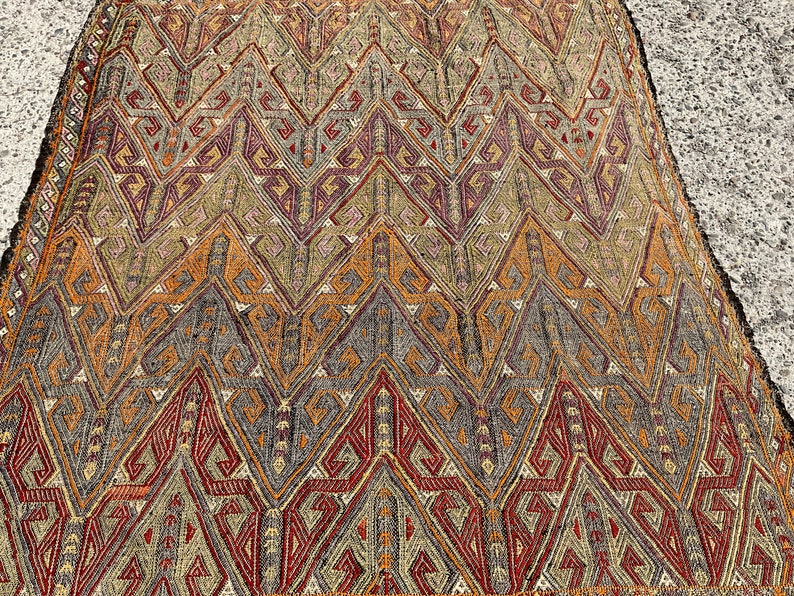 Pode incluir: Um close-up de um tapete tecido colorido com um padr&atilde;o geom&eacute;trico. O tapete &eacute; feito de l&atilde; e tem uma variedade de cores, incluindo vermelho, laranja, amarelo, verde e azul.