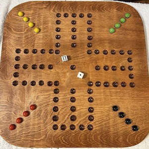 Puede incluir: Un tablero de juego de madera con una mancha marr&oacute;n. El tablero tiene una cuadr&iacute;cula de agujeros con canicas en ellos. Tambi&eacute;n hay dados y otras piezas de juego en el tablero.