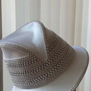 May include: A white hat with a wide brim and a silver beaded trim. The hat is made of a smooth, satin-like material.