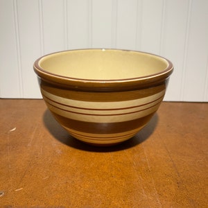 May include: A brown and cream striped ceramic mixing bowl. The bowl has a wide rim and a rounded bottom.