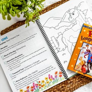 May include: An open spiral-bound book with text and a horse coloring page, next to a children's book titled "Pippi Longstocking". The book is on a woven mat with a small potted plant.