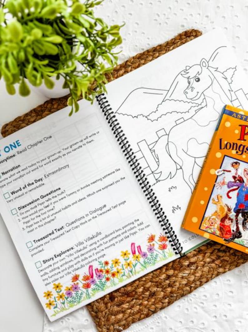 May include: An open spiral-bound book with text and a horse coloring page, next to a children's book titled "Pippi Longstocking". The book is on a woven mat with a small potted plant.