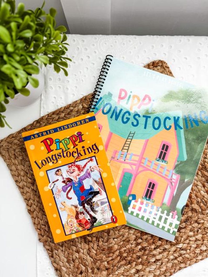 May include: Two children's books, "Pippi Longstocking" by Astrid Lindgren, and a spiral-bound book with the title "Pippi Longstocking" are displayed on a woven mat. The book covers feature colorful illustrations of Pippi and her house.