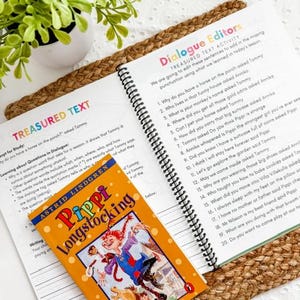 May include: An open book with spiral binding next to a children's book titled "Pippi Longstocking" by Astrid Lindgren. The book cover features a cartoon illustration of a girl. The text "Dialogue Editors" is visible.