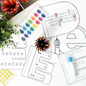 May include: A watercolor paint set with various colors, pencils, and educational worksheets with the letter "E" are arranged on a white surface. The worksheets include the text "Let's Play School".
