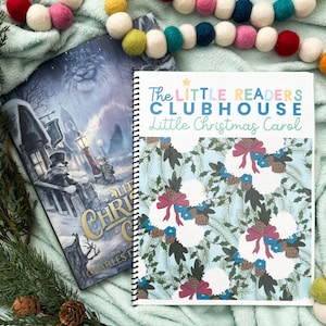 May include: A spiral-bound book titled "The Little Readers Clubhouse Little Christmas Carol" with a light blue cover featuring a floral design. A hardcover book with a winter scene is next to it. A colorful felt ball garland is draped across the scene.