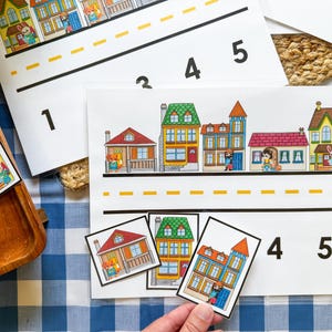 May include: A set of educational activity sheets and matching cards featuring colorful illustrations of houses and small animal characters. The sheets include a road graphic with dashed yellow lines and the numbers 1 through 5 printed in black.