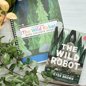 Könnte beinhalten: Zwei Bücher, "The Wild Robot" und ein "Book Explorer Guide", werden auf einer gestreiften Oberfläche gezeigt. Der Guide zeigt eine Waldszene und den Text "Let's Play School". Das Buchcover hat eine Waldillustration und den Titel "The Wild Robot".