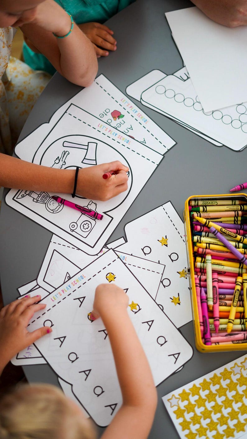 May include: Children's activity set with coloring pages and crayons. The pages feature illustrations and the text "LET'S PLAY SCHOOL". A yellow tin holds a variety of crayons. Gold star stickers are also present.