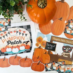 Op de afbeelding: Een speelset met pompoenveld-thema met bedrukte papieren borden met de tekst Pumpkin Patch en Pumpkin Patch Check-Out, diverse oranje pompoenuitsparingen en speelgeldbiljetten in coupures van één, vijf, tien en twintig dollar.