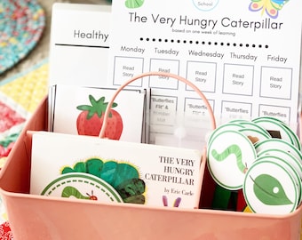 May include: A pink metal bin filled with educational materials for children. Includes a book titled "The Very Hungry Caterpillar" by Eric Carle, flashcards, and a weekly learning chart with a caterpillar and butterfly illustration.