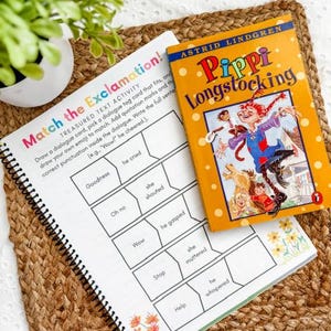 May include: A spiral-bound workbook with the title "Match the Exclamation!" sits next to a copy of "Pippi Longstocking" by Astrid Lindgren. The workbook has a colorful cover and prompts for matching dialogue tags. The book has an orange cover with illustrations.
