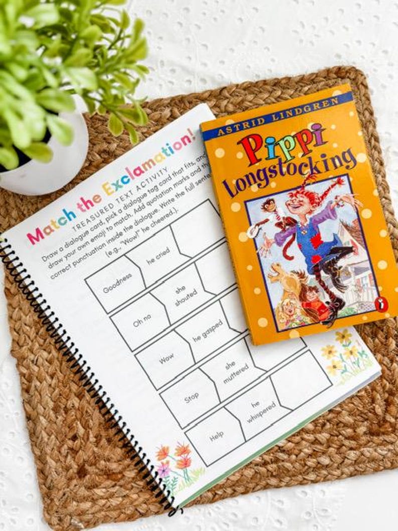 May include: A spiral-bound workbook with the title "Match the Exclamation!" sits next to a copy of "Pippi Longstocking" by Astrid Lindgren. The workbook has a colorful cover and prompts for matching dialogue tags. The book has an orange cover with illustrations.