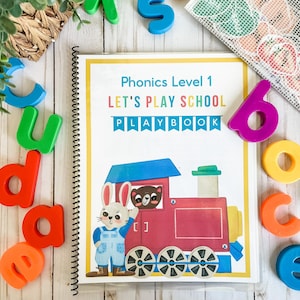 May include: A spiral-bound "Phonics Level 1 Let's Play School Playbook" with a colorful train illustration. The cover features a rabbit and bear. Colorful magnetic letters and numbers surround the book, including the letters "d", "u", "d", "e", "c", and "o".