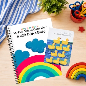 May include: A spiral-bound workbook titled Let's Play School My First School Curriculum 10 Little Rubber Ducks with a rainbow and cloud graphic, alongside a small book titled 10 Little Rubber Ducks by Eric Carle featuring ten yellow rubber ducks.