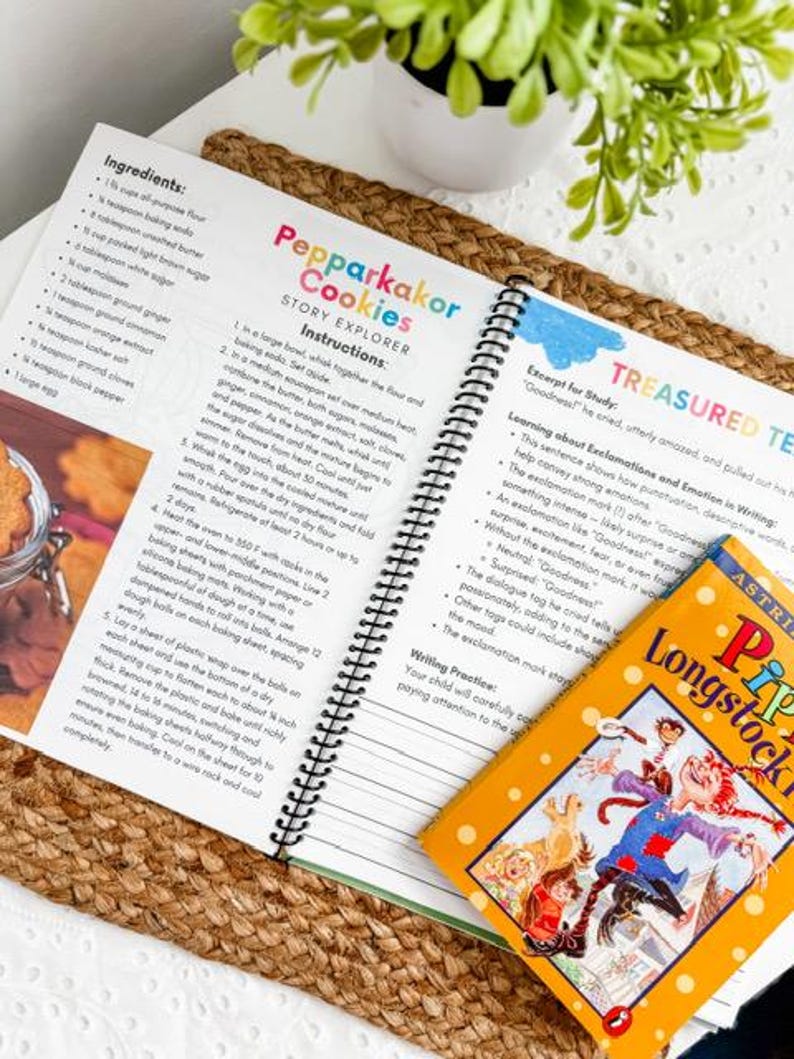 May include: An open cookbook with a spiral binding displays a recipe for "Pepparkakor Cookies." A colorful children's book titled "Pippi Longstocking" rests on the page. The image is set on a woven mat with a small potted plant.