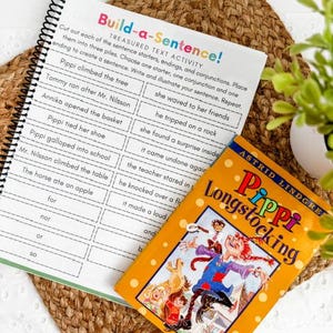 May include: A spiral-bound workbook with the title "Build-a-Sentence!" and a colorful cover of the book "Pippi Longstocking" by Astrid Lindgren, resting on a woven mat. The workbook features sentence-building exercises.
