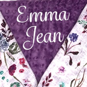 Puede incluir: Manta de beb&eacute; de color morado y blanco con un patr&oacute;n floral y el nombre "Emma Jean" bordado en el lado morado.