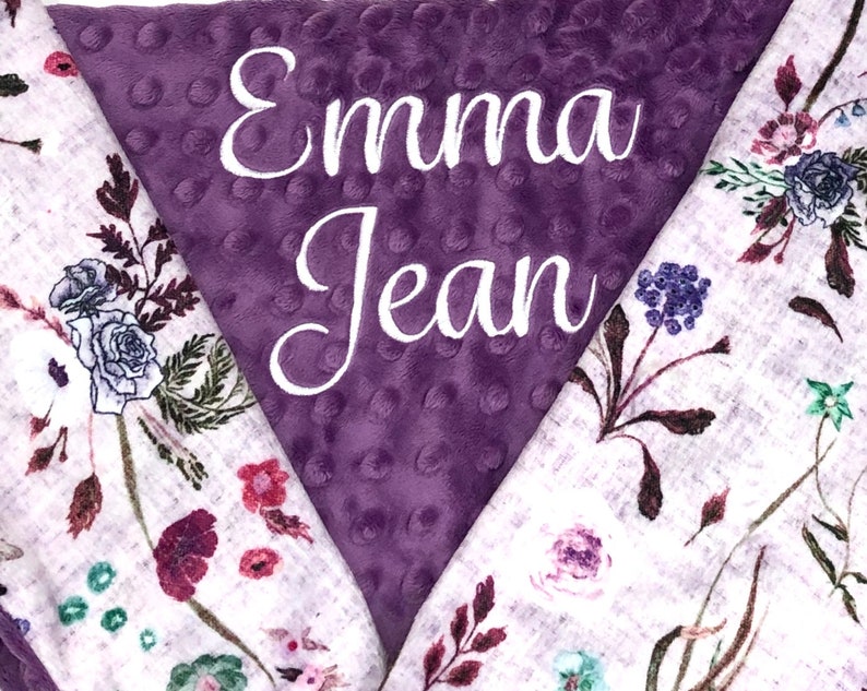 Puede incluir: Manta de beb&eacute; de color morado y blanco con un patr&oacute;n floral y el nombre "Emma Jean" bordado en el lado morado.
