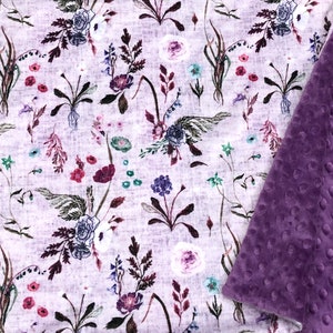 Puede incluir: Una suave manta de beb&eacute; con estampado floral blanco y morado, con un respaldo de minky morado de felpa.