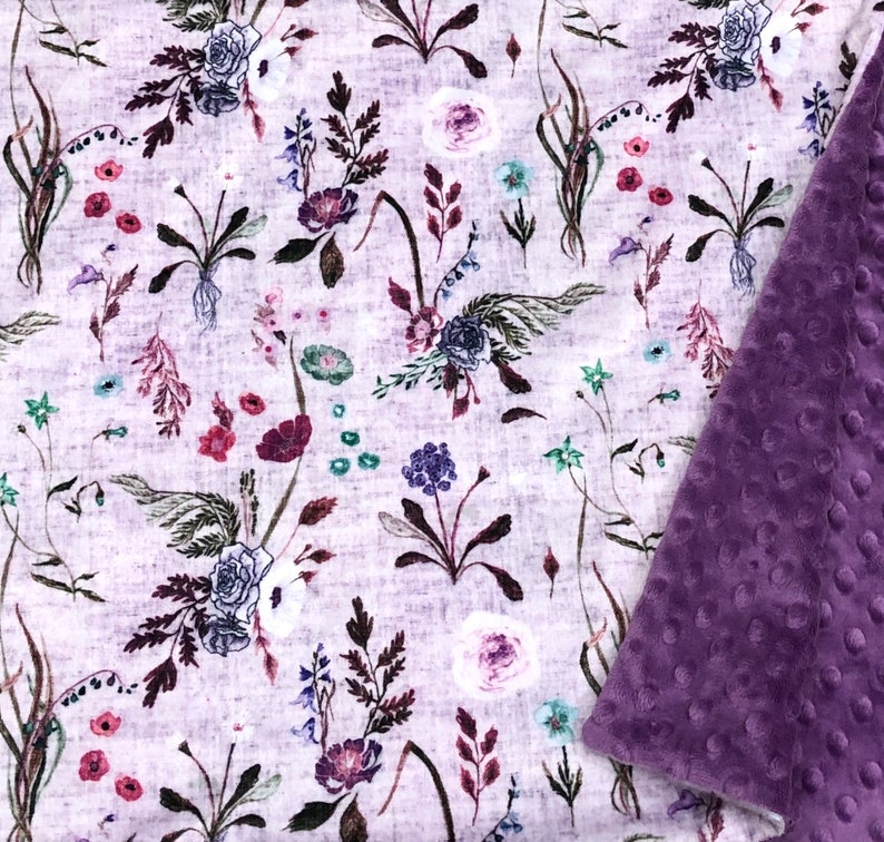 Puede incluir: Una suave manta de beb&eacute; con estampado floral blanco y morado, con un respaldo de minky morado de felpa.