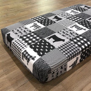 May include: Black and white patchwork dog bed cover with a cow print design. The cover features a variety of patterns, including plaid, stripes, and wood grain.