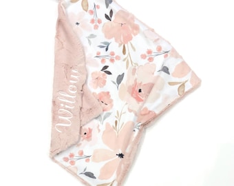 May include: A soft baby security blanket featuring a white fabric side with a floral pattern in shades of pink, peach, and grey. The reverse side is a textured dusty pink fabric embroidered with the name Willow and two satin ribbon tags.