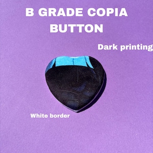 May include: A heart-shaped button with a dark print and a white border, set against a purple background. The text "B GRADE COPIA BUTTON" and "Dark printing" are also visible.