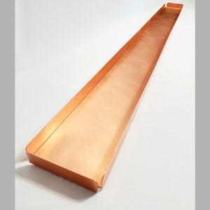 May include: A long, rectangular copper tray with a slightly curved edge. The tray is empty and has a smooth, polished surface.
