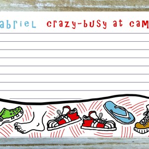 May include: A lined notepad with the words "Gabriel crazy-busy at camp!" in blue and red. The bottom of the page features cartoon illustrations of shoes, sandals, and a foot. The background is a light wood grain.