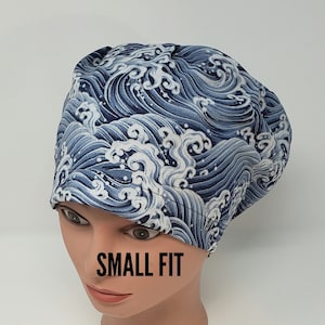 May include: A blue and white wave-patterned scrub cap with the text "SMALL FIT" in black. The cap is on a mannequin head. The fabric design features stylized ocean waves.