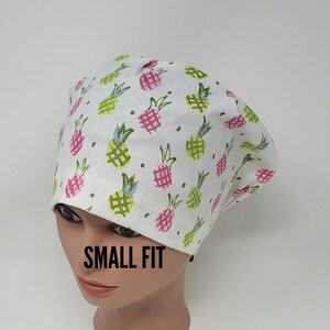 May include: White scrub hat with a pineapple print. The hat is labelled "SMALL FIT".