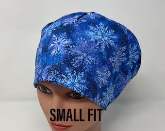 Könnte beinhalten: Eine blaue OP-Haube mit Schneeflockenmuster. Die Haube ist aus Stoff gefertigt und trägt den Aufdruck "SMALL FIT". Die Schneeflocken sind weiß, vor einem blau-violetten Hintergrund.