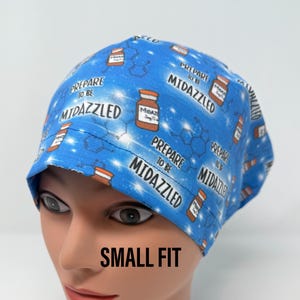 May include: Blue surgical scrub hat with a white background and a repeating pattern of medicine bottles and the text "Prepare to be Midazzled". The hat is labelled "Small Fit".